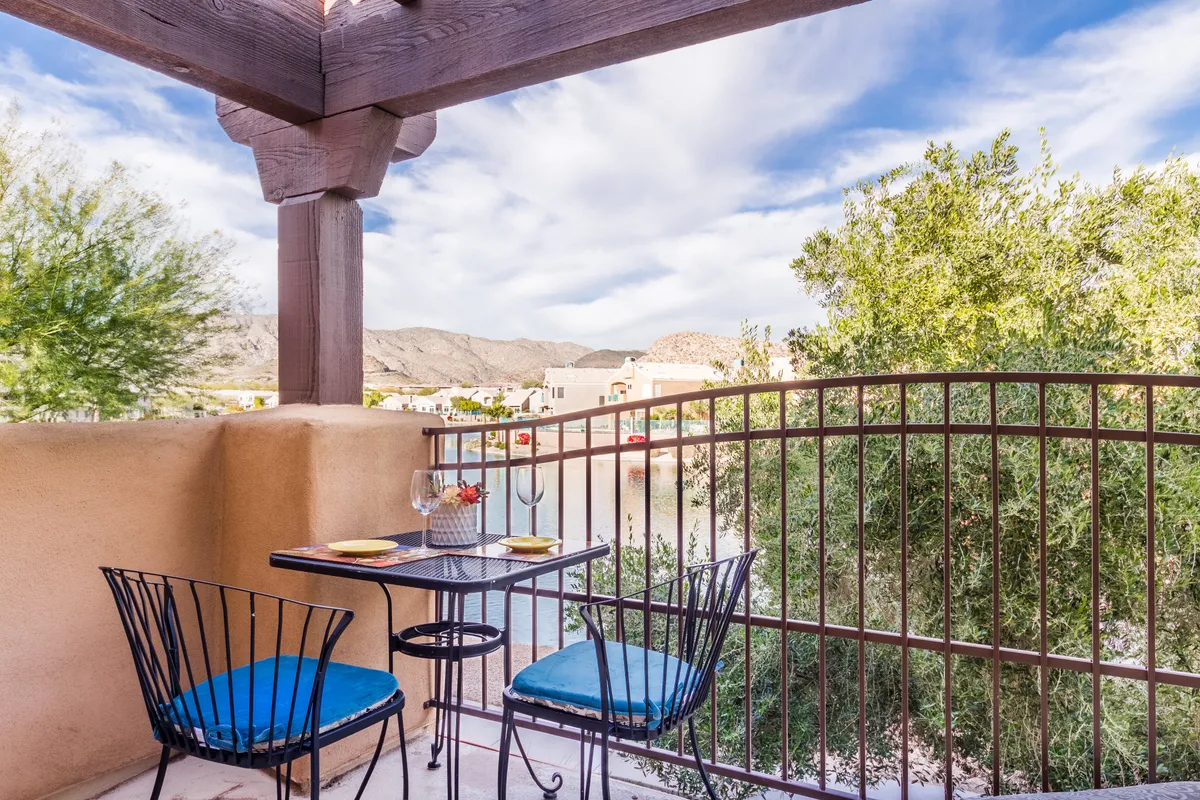 This exterior image features a decorative railing and a small dining table set on a patio or balcony, with a scenic view of mountains and water in the background. The tranquil setting invites relaxation and outdoor enjoyment, suggesting the proximity to the lake.