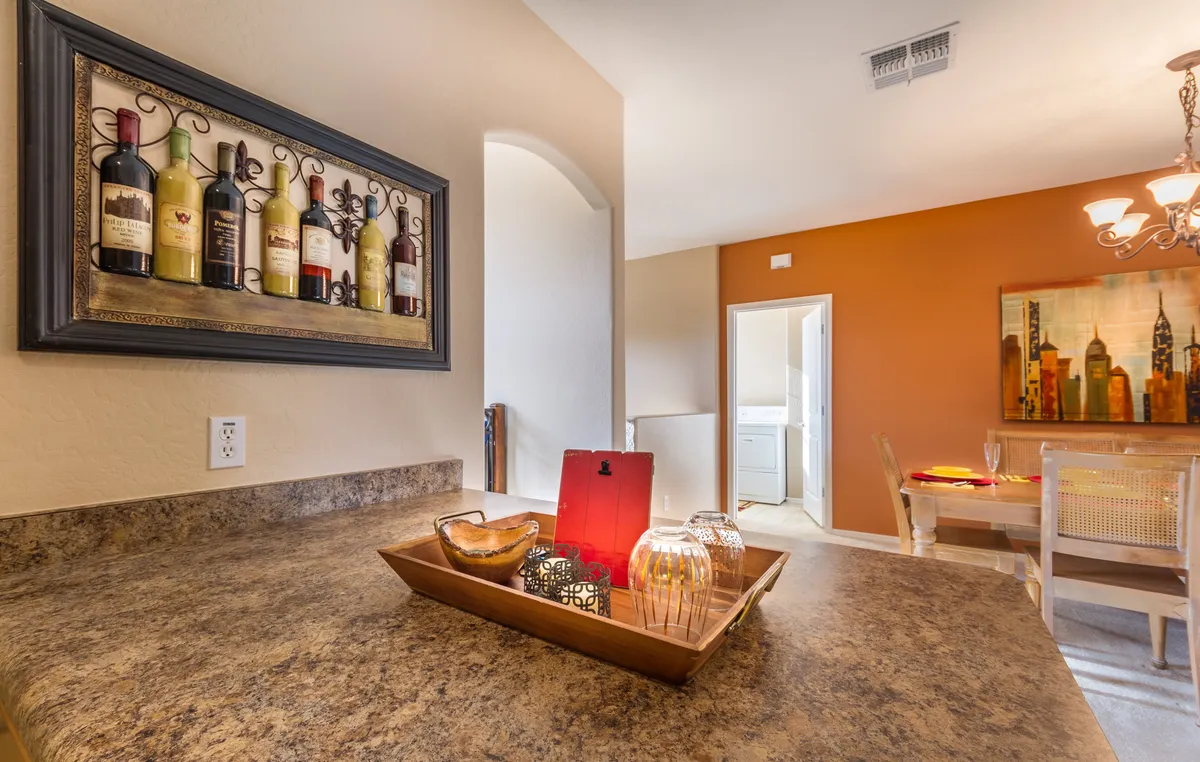 The photo displays a dining area adorned with wine bottle artwork and a decorative tray with candles, set against a warm, welcoming backdrop. The setup hints at intimate dinners, celebrating milestones, and sharing laughter, enhancing the sense of romance and togetherness.