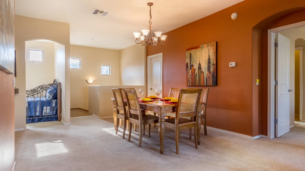 This image features a dining table elegantly set with plates and glasses, a sparkling chandelier overhead, and tasteful artwork on the wall. The overall ambiance is warm and welcoming, inviting both intimate family dinners and celebratory gatherings.