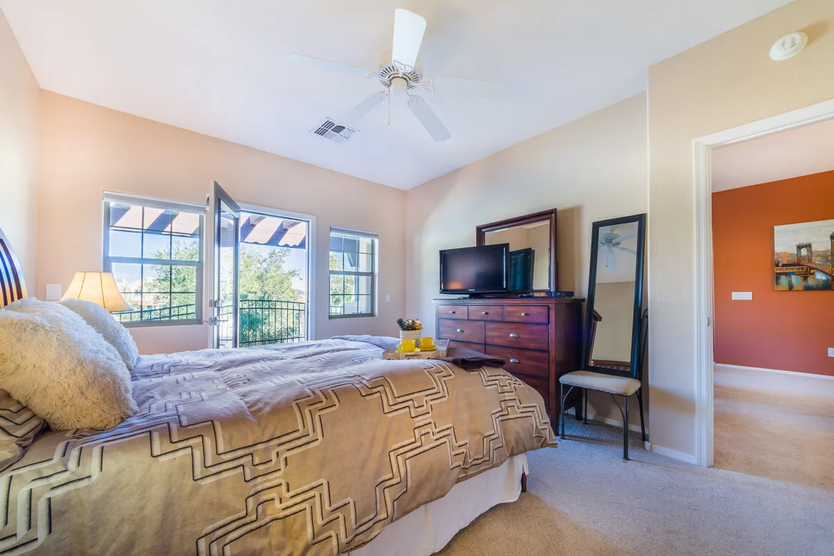 A bright bedroom with a decorative blanket on the bed, large windows that allow abundant sunlight, and a dresser topped with a television. The room feels airy and welcoming, providing a restful spot to unwind after a day of adventure.