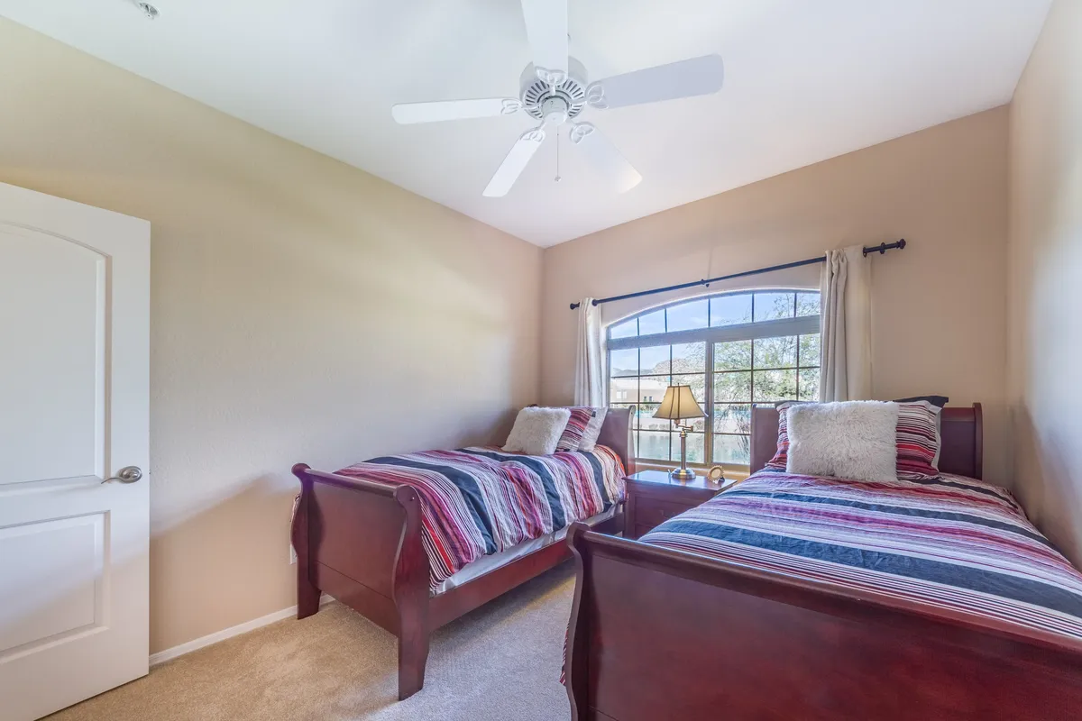 A cheerful second bedroom with two twin beds dressed in colorful striped bedding. Natural light floods the space through a window, and a bedside lamp offers coziness. The setup is inviting for both children and guests, with a playful yet comfortable atmosphere.