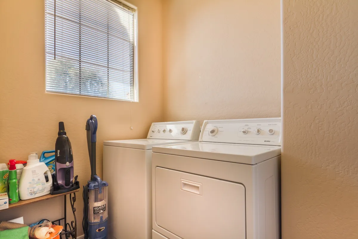 A tidy laundry area featuring a washing machine, dryer, and a window bringing in natural light, complemented by organized cleaning supplies. The space feels practical, convenient, and family-friendly.