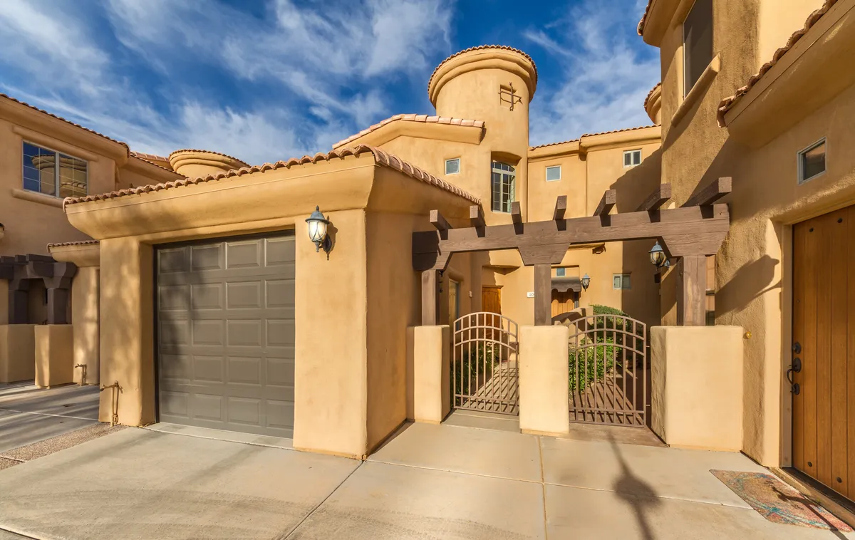 An exterior view of the residence, highlighting the garage door, arched entrance, decorative gate, and the architectural details of the facade. The scene conveys an inviting approach and a sense of arrival.